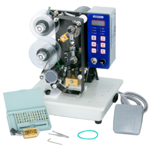 Frontal de la impresora digital semiautomática JORESTECH de estampado en caliente con foil y su pedal. La máquina tiene instalado el rodillo de tinta caliente. También se muestra el juego completo de tipos, las herramientas de instalación y un portatipos incluidos con la máquina