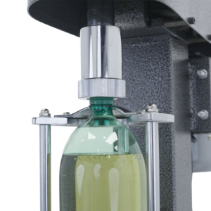 Primer plano de la encorchadora semiautomática gris JORES TECHNOLOGIES® con una botella de plástico verde llena de líquido verde insertada. La encorchadora está enroscando la tapa en la botella verde.