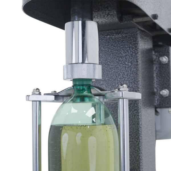 Primer plano de la encorchadora semiautomática gris JORES TECHNOLOGIES® con una botella de plástico verde llena de líquido verde insertada. La encorchadora está enroscando la tapa en la botella verde.