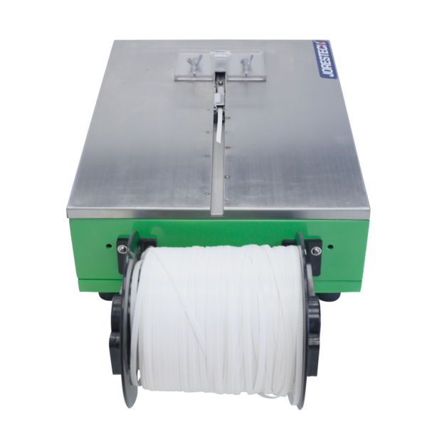 Vista superior de la máquina flejadora de sobremesa JORES TECHNOLOGIES® que muestra la mesa de trabajo de acero inoxidable de la máquina. El rollo de fleje está instalado en la máquina.