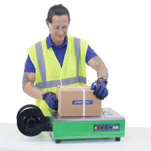 Trabajador usando la máquina de flejado y enfajado de sobremesa JORES TECHNOLOGIES® para asegurar una caja de cartón para envío