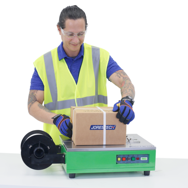Trabajador usando la máquina de flejado y enfajado de sobremesa JORES TECHNOLOGIES® para asegurar una caja de cartón para envío