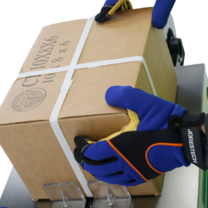 primer plano de una caja de cartón que ha sido protegida con flejes blancos de polipropileno para envío. La máquina ha sido embalada utilizando una flejadora semiautomática de perfil bajo JORES TECHNOLOGIES®