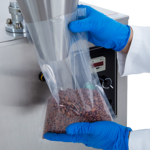 Primer plano de las manos de una persona sosteniendo una bolsa de plástico transparente debajo del cono dosificador de la llenadora volumétrica semiautomática mientras libera 1000 ml de frijoles de flujo libre con precisión