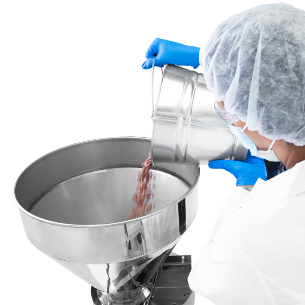 Un trabajador que lleva guantes de nitrilo azules y una variedad de equipos de protección personal dispensando frijoles en la tolva de acero inoxidable del llenador volumétrico semiautomático JORES TECHNOLOGIES®