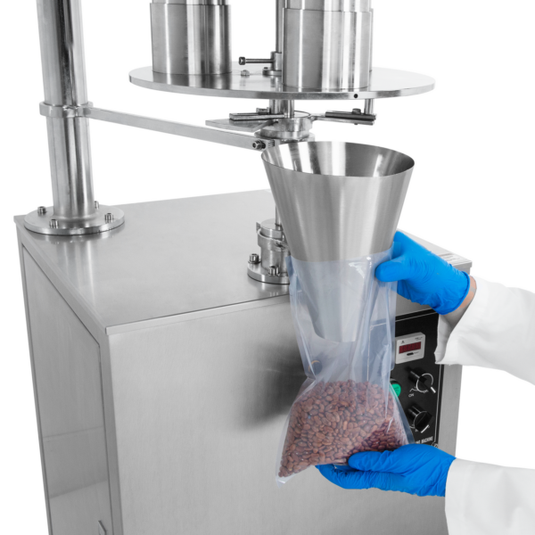 Primer plano de las manos de una persona sosteniendo una bolsa de plástico transparente bajo el cono de dosificación del llenador volumétrico semiautomático mientras libera 500 ml de producto de flujo libre con precisión dentro de la bolsa