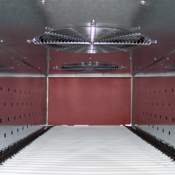 Detalle del interior del horno de termorretracción mostrando la cámara de calentamiento, paredes perforadas de acero inoxidable, rejillas de acero inoxidable para los ventiladores de calentamiento, un transportador de rodillos y la cortina de salida del túnel de calor de la túnel envolvedora Jorestech de 20 x 12 pulgadas