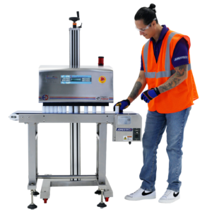 Un operador que lleva un chaleco naranja de alta visibilidad puede verse colocando envases blancos sobre una cinta transportadora para que puedan ser sellados por una selladora por inducción para tapas