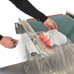 trabajador usando la selladora térmica semiautomática en L de acero inoxidable con transportador para empaquetar lotes de envases plásticos de tamaño mediano.