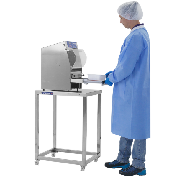Persona que lleva ropa de PPE desechable y guantes usando una selladora de bandejas colocada sobre una mesa de trabajo de preparación de acero inoxidable JORES TECHNOLOGIES®