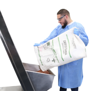 Trabajador vertiendo una gran bolsa de frijoles secos en un elevador de cubeta simple de acero inoxidable
