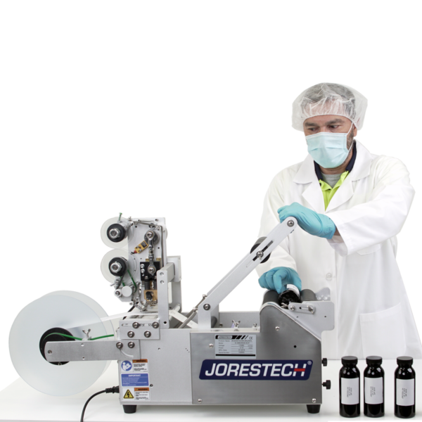 Un hombre que lleva equipo de protección personal. Está operando la etiquetadora semiautomática JORES TECHNOLOGIES® aplicando etiquetas a recipientes redondos. Se muestra un conjunto de 3 botellas con etiquetas impresas que contienen información escrita