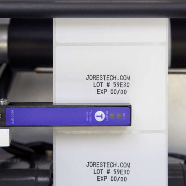primer plano del sensor y la etiqueta impresa con el nombre de la marca, número de lote y fecha de producción en un aplicador de etiquetas semiautomático con impresora integrada