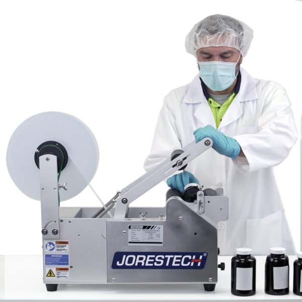 Hombre que lleva equipo de protección personal mientras opera la máquina etiquetadora semiautomática JORES TECHNOLOGIES® empujando la palanca de activación para aplicar etiquetas a envases redondos