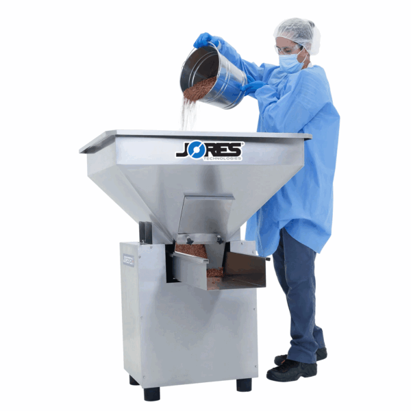 Un trabajador vertiendo granos rojos en la tolva de una alimentadora vibratoria de tolva de acero inoxidable JORES TECHNOLOGIES®.
