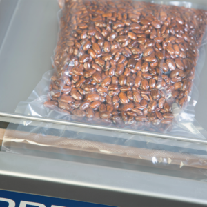 Detalle de una bolsa al vacío sellable con frijoles rojos después de usar la envasadora al vacío comercial de cámara de sobremesa de acero inoxidable con una barra de sellado. También se puede apreciar el sellado de la bolsa al vacío, así como su posición en la barra de sellado.