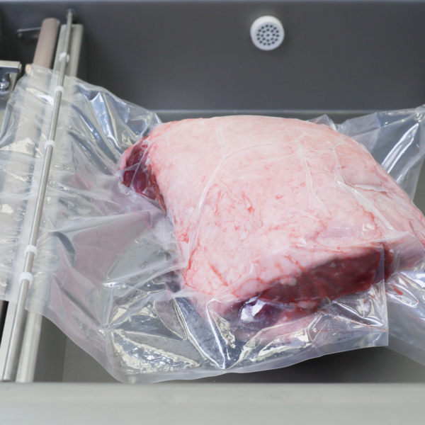 Bolsa sellada al vacío con un gran trozo de carne en su interior. La bolsa está colocada dentro de la cámara de la selladora al vacío comercial de sobremesa JORES TECHNOLOGIES® de una sola cámara, de acero inoxidable, con doble barra de sellado