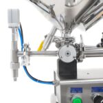 Primer plano que muestra el detalle de la boquilla antigoteo, el cilindro del pistón, la tolva calefactada y parte del panel de control del llenador de pasta de sobremesa con pistón