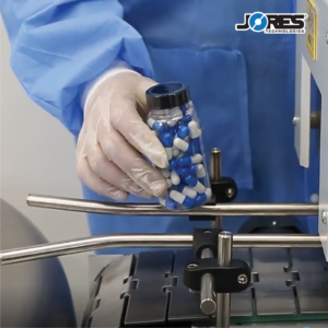 primer plano de una persona introduciendo un envase transparente con pastillas azules y blancas en un túnel termorretráctil de precinto inviolable