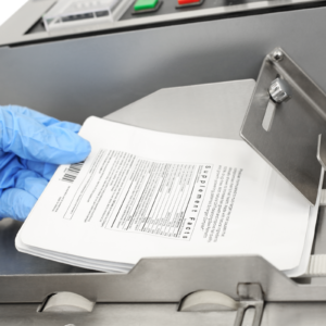 Primer plano de la mano de una persona colocando un grupo de bolsas de plástico blancas en la codificadora de rodillo de tinta caliente de mesa JORES TECHNOLOGIES® para que la máquina pueda comenzar a codificar