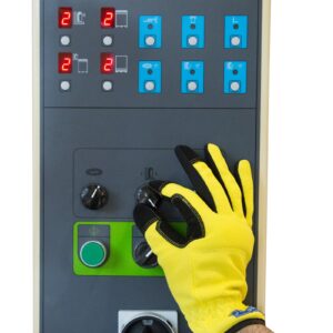 La mano de un trabajador con guante protector amarillo ajustando uno de los botones de control tipo dial en el panel de control de una envolvedora de palets con plataforma giratoria y preestirado