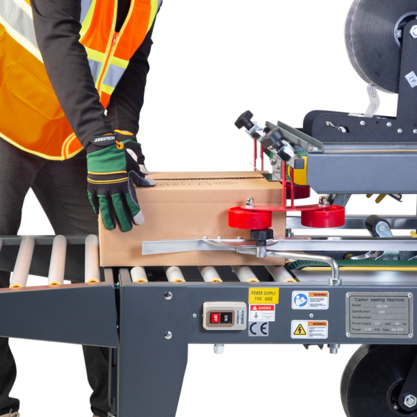 Operador introduciendo una caja marrón en la selladora de cajas semiautomática. La máquina aplica cinta autoadhesiva en la parte superior e inferior de las cajas en cada pasada.