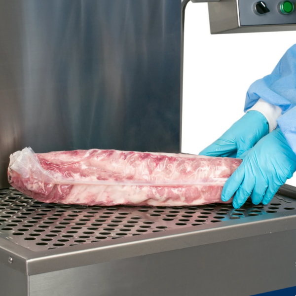 Manos de una persona con ropa protectora desechable retirando un rack de costillas con film retráctil envasado al vacío del tanque de agua de una máquina termorretráctil de agua caliente tipo inmersión semiautomática JORES TECHNOLOGIES®