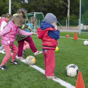 Un grupo de niños jugando en un campo marcado con varios conos naranjas de entrenamiento deportivo