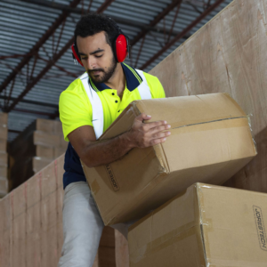 Un hombre lleva orejeras rojas JORESTECH con cancelación de ruido mientras carga cajas en una fábrica