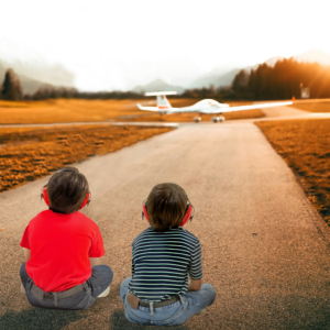 2 niños usando orejeras de protección auditiva mientras observan aviones despegar y aterrizar desde un aeropuerto