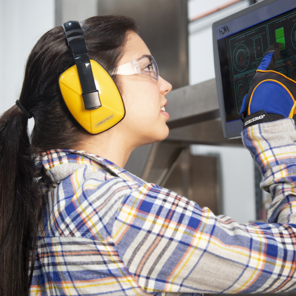 Una mujer con gafas de seguridad, guantes y orejeras de protección auditiva JORESTECH mientras opera una máquina grande y ruidosa