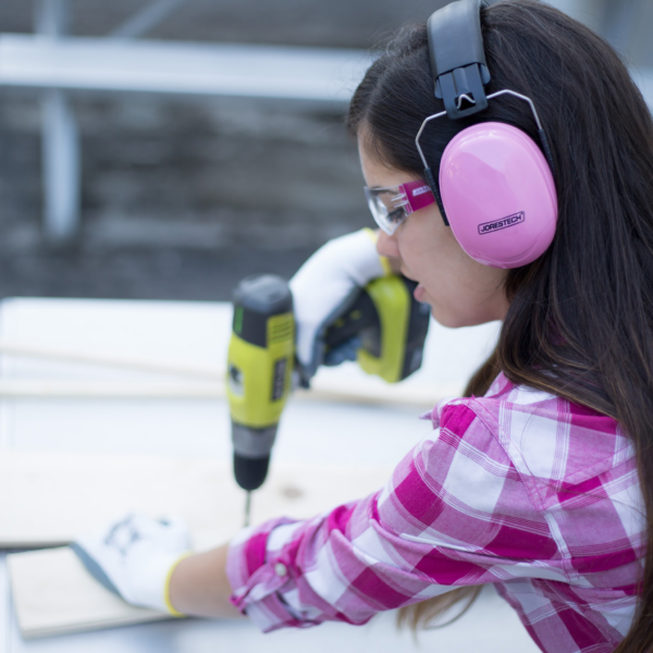 Mujer usando orejeras de protección auditiva rosas con cancelación de ruido y banda para la cabeza plegable mientras opera una herramienta eléctrica ruidosa