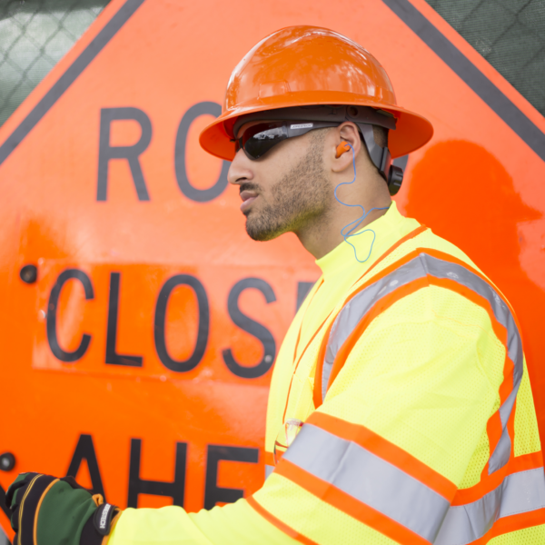 Un trabajador con tapones para los oídos para protección auditiva, ropa de alta visibilidad y casco de seguridad durante una obra de construcción vial