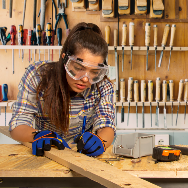Una mujer que lleva gafas de seguridad ventiladas antivaho mientras trabaja con madera y herramientas para madera en su estudio de arte