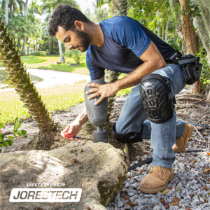 Un electricista con rodilleras JORESTECH rellenas de gel, arrodillado sobre piedras mientras repara una luz de jardín