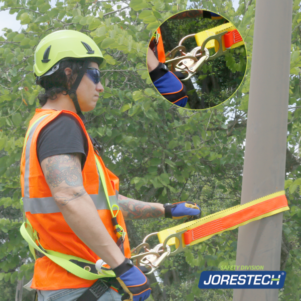 Un trabajador usando la correa de anclaje para brazo cruzado JORESTECH con doble anillo para sujetarse a una estructura redonda. El hombre lleva casco, ropa de alta visibilidad y la correa cross armor está enganchada a su arnés de 3 anillas en D.