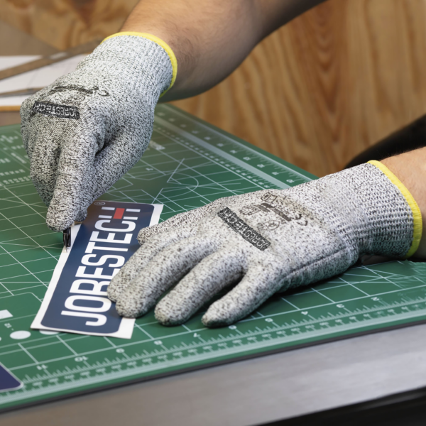 Trabajador usando el guante de seguridad multiusos Jorestech mientras corta un trozo de papel con un cúter de precisión