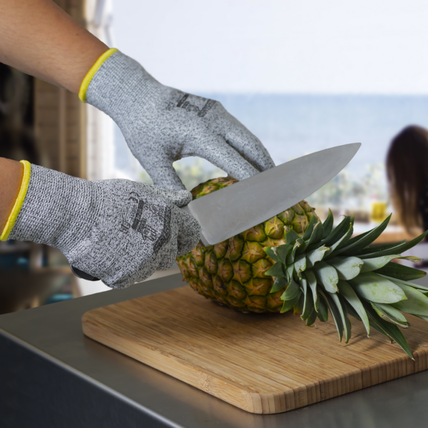 Persona que lleva el guante de trabajo de seguridad multipropósito Jorestech mientras sostiene un cuchillo de chef para cortar la corona de una piña