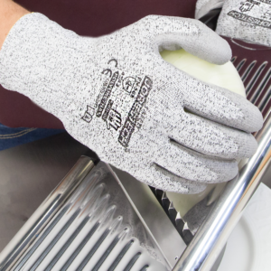 Persona que lleva los guantes de trabajo de seguridad JORESTECH grises resistentes a cortes con palma recubierta de poliuretano mientras corta una cebolla con una cortadora de hojas de metal plateado