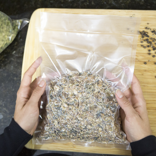 Persona manipulando una bolsa JORESTECH sellada al vacío con relieve, con té o especias en su interior, en una cocina usando una tabla de cortar marrón