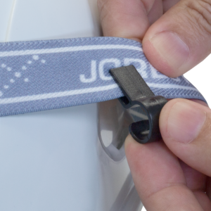 Primer plano de una persona insertando la correa elástica de una linterna frontal en el clip para linterna frontal de casco Jorestech, que irá colocado en un casco de seguridad