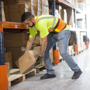 Un trabajador que lleva un cinturón de soporte lumbar ajustable de alta visibilidad y alta resistencia mientras organiza cajas dentro de estanterías de almacenamiento en un almacén