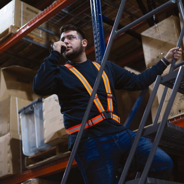 Un trabajador que lleva un arnés de seguridad ajustable naranja mientras está en la parte superior de una escalera