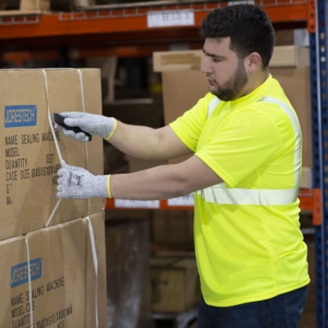 Imagen de un hombre usando una camisa de seguridad amarilla/lima JORESTECH mientras retira correas de cajas mientras trabaja en un almacén