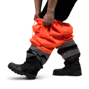 Una persona poniéndose los pantalones impermeables de seguridad JORESTECH naranjas y negros como capa de protección contra la lluvia sobre su propia ropa