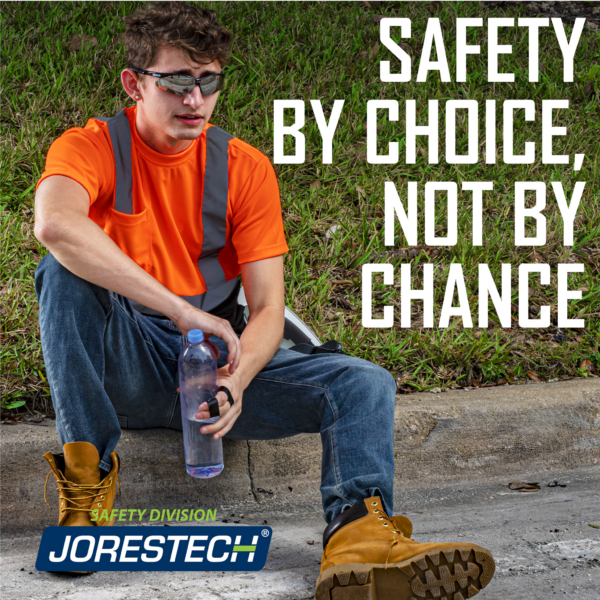 Trabajador que lleva una camisa de seguridad naranja y negra JORESTECH. Está sentado en el suelo con una botella de agua refrescándose en una obra de construcción. Un texto dice: la seguridad por elección, no por casualidad.