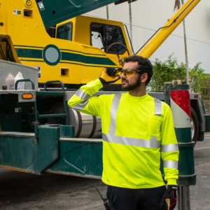 Trabajador vistiendo una camisa de seguridad de alta visibilidad amarilla de manga larga mientras opera un gran camión verde al fondo