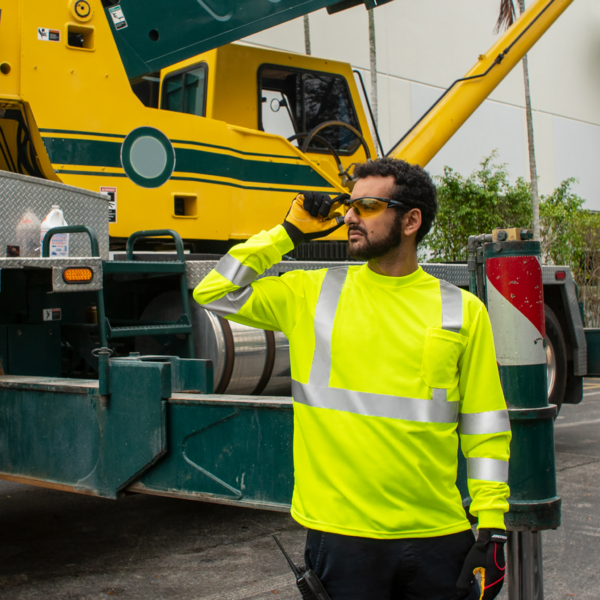 Trabajador vistiendo una camisa de seguridad de alta visibilidad amarilla de manga larga mientras opera un gran camión verde al fondo