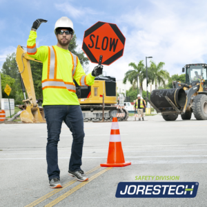 Un hombre lleva la camiseta de seguridad JORESTECH con franjas amarillas y naranjas mientras dirige el tráfico debido a una gran reparación de la carretera.