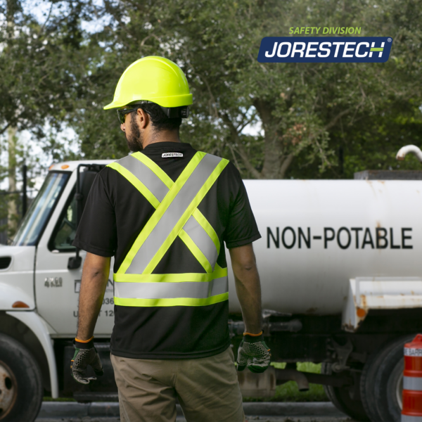 Un hombre que lleva una camisa de seguridad reflectante jorestech de manga corta negra y lima mientras está de pie junto a un camión